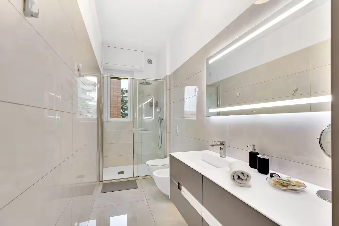 Bagno con mobile lavabo, specchio illuminato e doccia in vetro