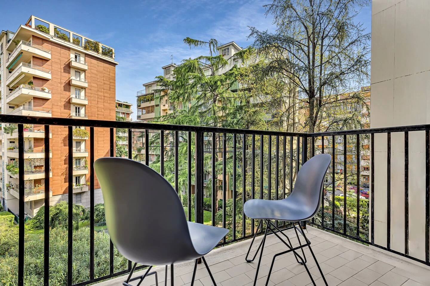 Balcone arredato con due sedie, affacciato sugli alberi e sui palazzi