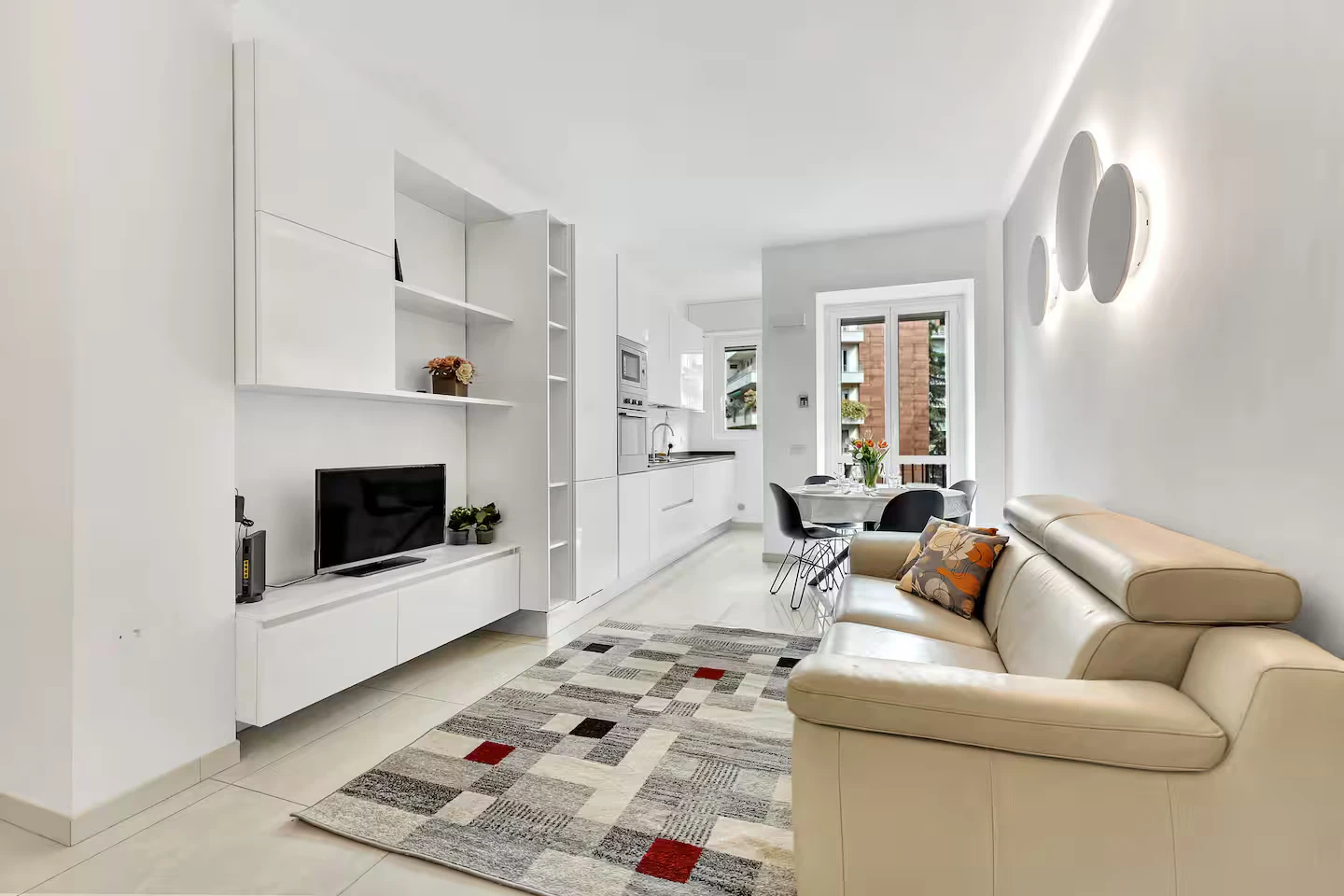Zona giorno luminosa con divano letto, smart TV e cucina sullo sfondo